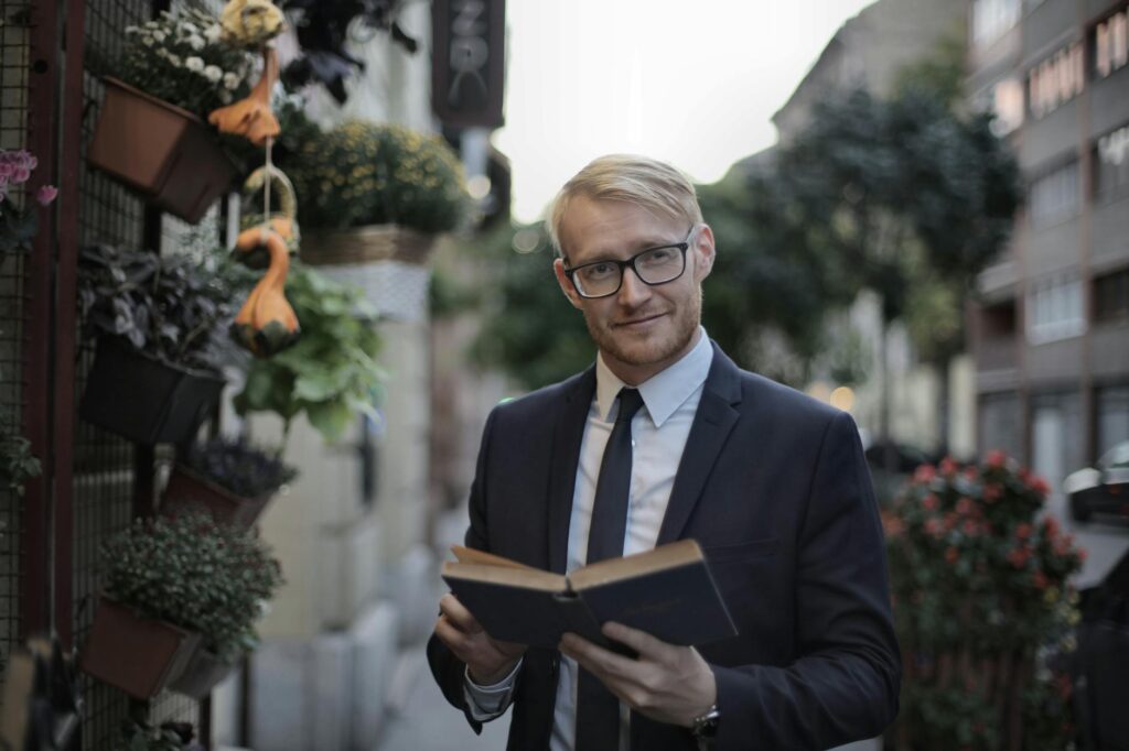 smiling bearded man in formal wear reading book in street